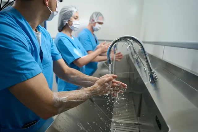 Clinical staff washing hands at a stainless steel sink